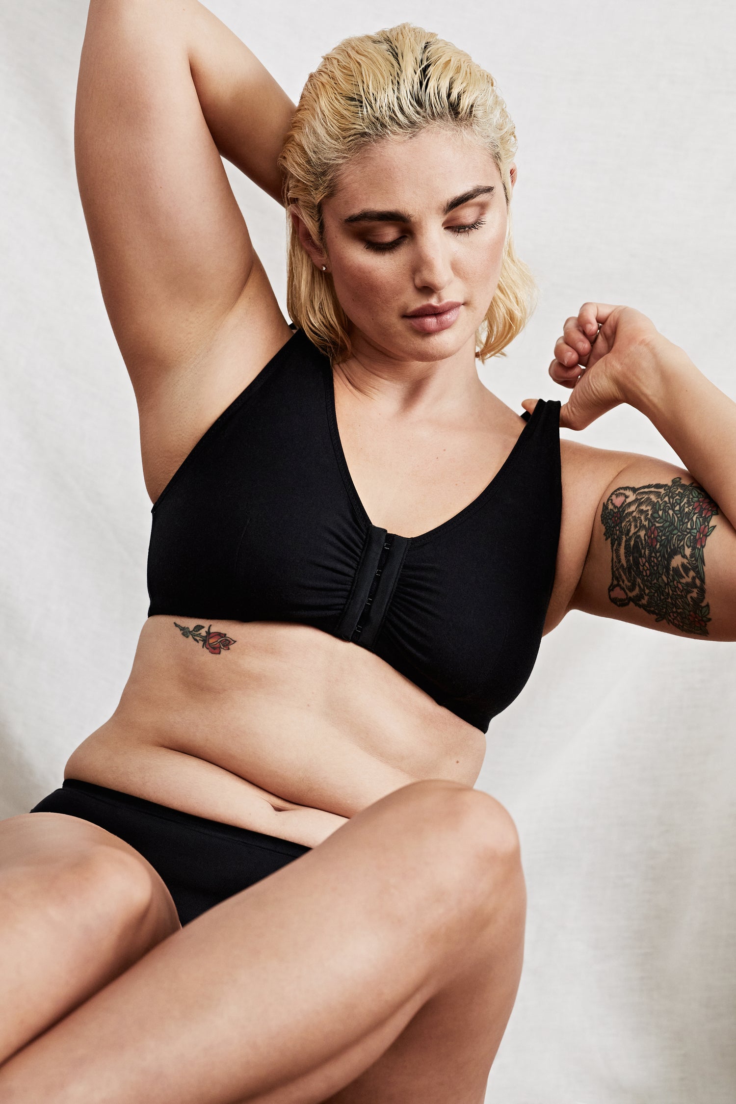 Model lounging comfortably in a black front closure Myya bra, designed for post-surgery support with soft, breathable fabric and a non-wired, secure fit.